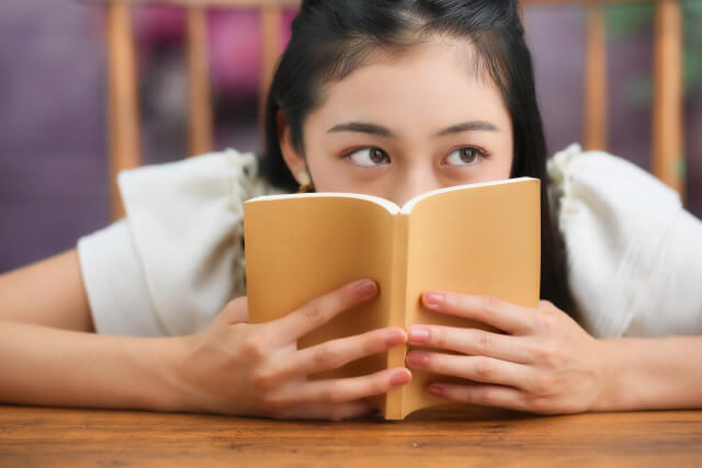 本で口元を隠す横目の女性